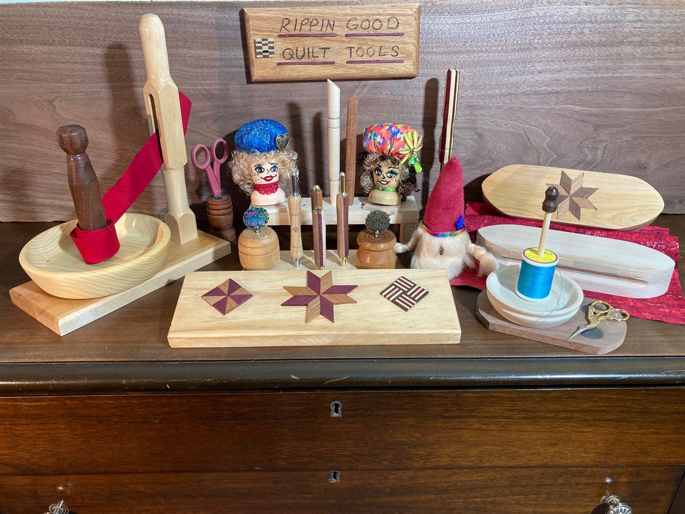 A display of Rippin' Good quilt tools: a binding bowl, seam rippers, clappers, pincushions and a thread stand under the wooden shop sign